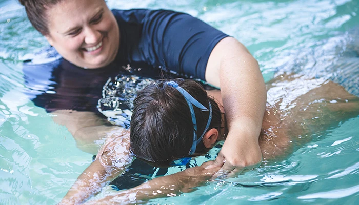 Instructor helping child swim in pool